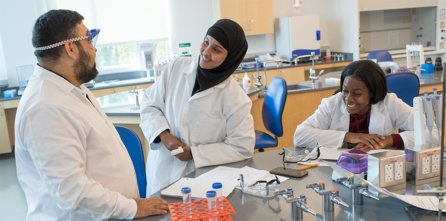 Roderico Acevedo, assistant professor at Westfield State University in Massachusetts, talks with biology majors (now graduates), from left, Hibo Hussein and Emmanuela Frimpong, in a college laboratory in spring 2019.