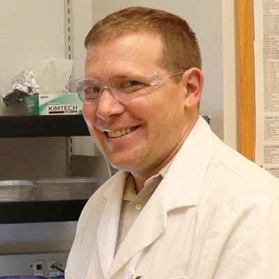 Portrait of Ryan Jackson in the lab wearing goggles and lab coat