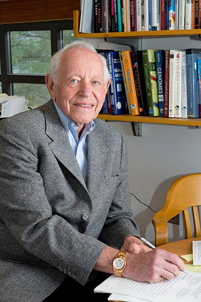 Leon Rosenberg seated and writing in front of books