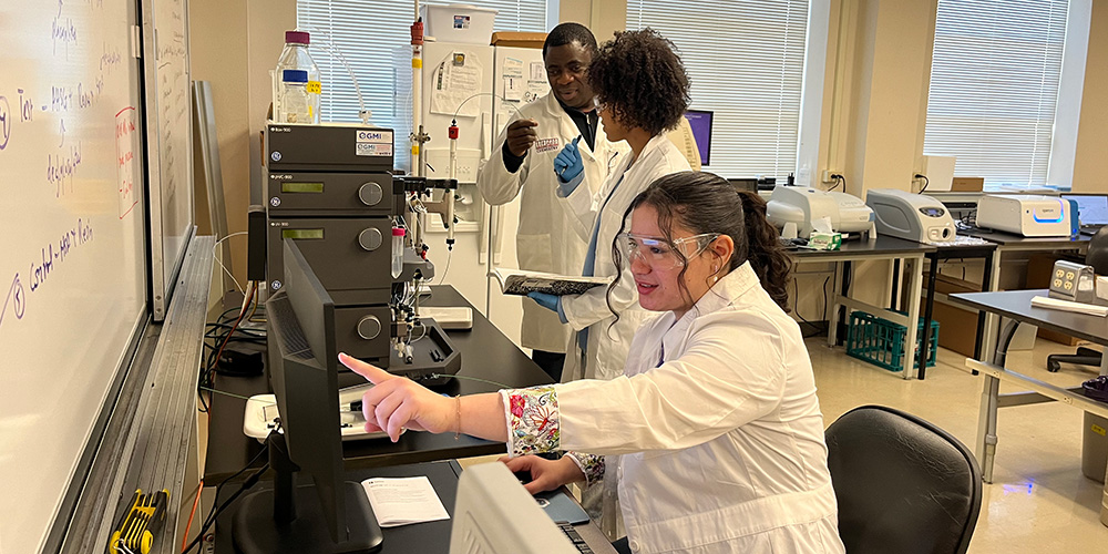 Tayo Odunuga looks on as senior biochemistry students Ravyn Solis and Madison McFarland check out information on a computer screen in the lab.