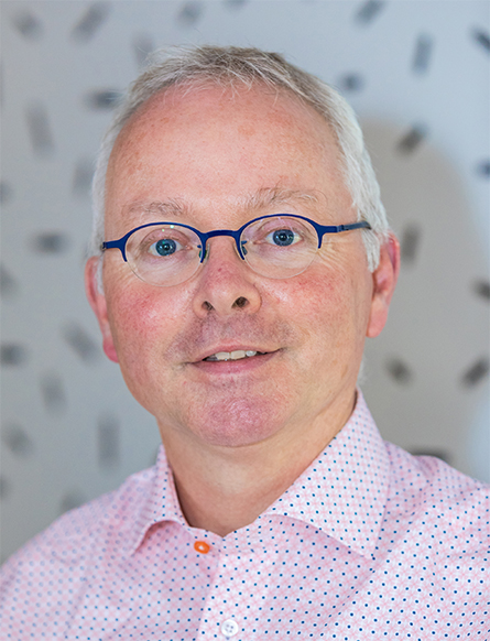 A portrait of Albert Heck. He has short gray hair, half-rimmed glasses, and a pink and blue checked Oxford shirt.