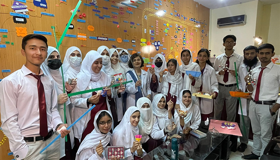 Fatahiya Kashif (in white lab coat) shows visitors the metabolic pathways map she and her students created on the wall of her office at the Federal Medical College in Islamabad.